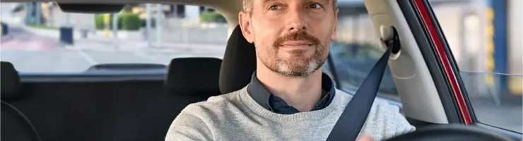 Un homme barbu au regard confiant conduit sa voiture, portant sa ceinture de sécurité.