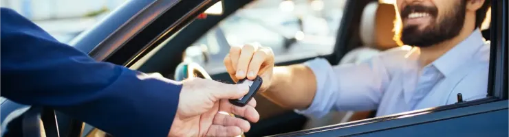 Un homme souriant dans une voiture reçoit les clés d'une autre personne.