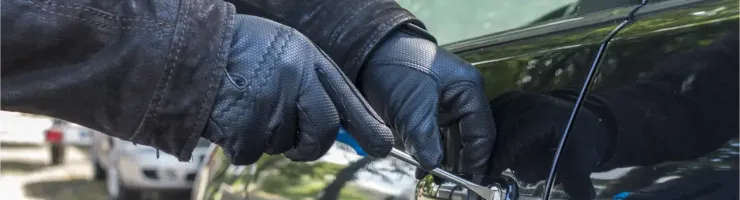 Des mains gantées essaient de forcer la serrure d'une portière de voiture noire.