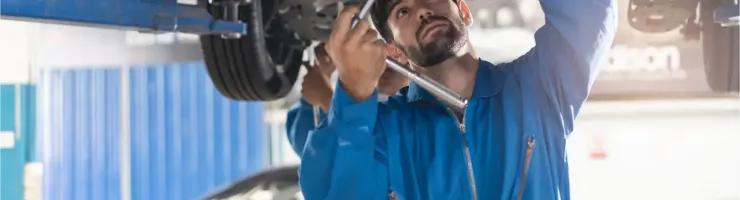 Deux mécaniciens en combinaison bleue travaillent sous une voiture surélevée dans un garage.