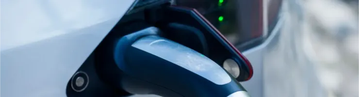 Gros plan sur un chargeur branché sur une voiture électrique blanche, avec des voyants verts allumés.