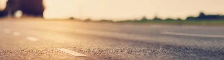 Gros plan sur une route asphaltée au coucher du soleil, avec des marques au sol et un arrière-plan flou.