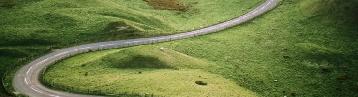 Vue aérienne d'une voiture sur une route sinueuse traversant des collines verdoyantes.