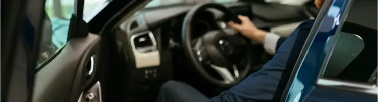 Un homme en costume entre dans une voiture, main sur la portière et l'autre sur le volant.