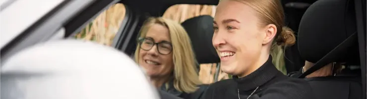 Une jeune femme dans une voiture, mains sur le volant, avec sa mère côté passager.