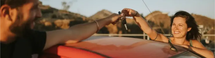 Un homme donne les clés de voiture à une femme souriante, adossée à une voiture rouge.