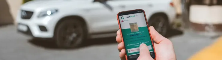 Une personne utilise l'application Certimat sur son téléphone pour la demande en ligne de carte grise d'une voiture blanche, garée en arrière-plan.
