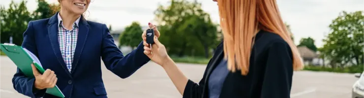 Une femme en costume remet des clés de voiture à une autre femme dans un parking.