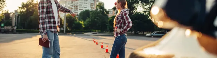 Deux jeunes en chemises à carreaux se font face sur un parking, des cônes de signalisation sont visibles.