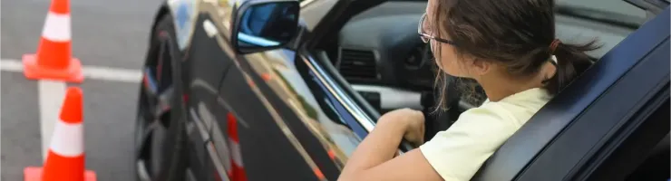 Une personne regarde par la fenêtre d'une voiture noire avec des cônes de circulation à côté.