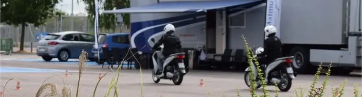 Deux personnes conduisent des scooters sur une piste de formation, avec un grand camion en arrière-plan.