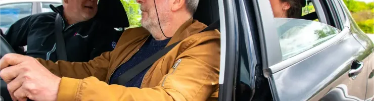 Trois personnes dans une voiture, un homme au volant regardant sur le côté.