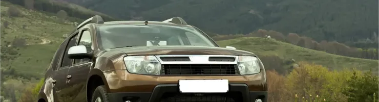 Un SUV marron est garé sur une colline herbeuse avec des montagnes en arrière-plan sous un ciel nuageux.