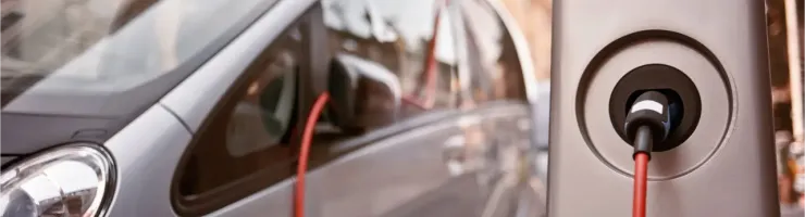 Une voiture électrique grise est branchée à une borne de recharge dans une rue de ville.