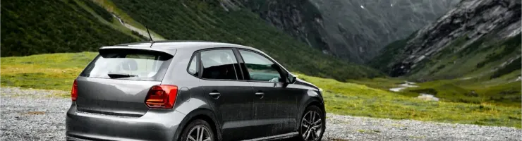Une voiture grise anthracite est garée sur un chemin de gravier avec un paysage montagneux spectaculaire derrière elle.