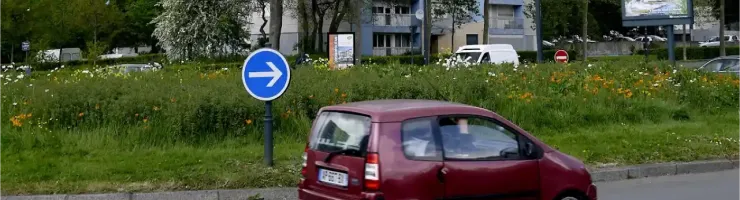 Une voiturette rouge circule sur la route d'un quartier où est visible plusieurs immeubles.