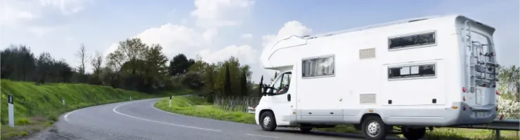 Un grand camping-car blanc roule sur une route sinueuse à travers la campagne, sous un ciel bleu parsemé de nuages blancs.