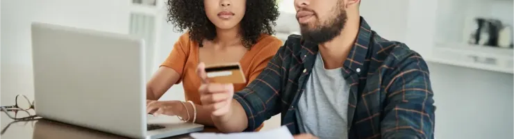 Un couple est assis à une table devant un ordinateur portable, la femme tenant une carte de crédit pendant qu'ils gèrent leurs finances.