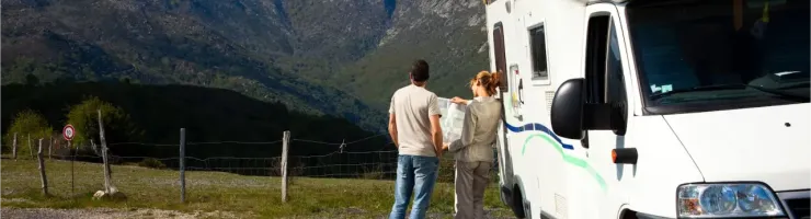 Un couple regarde un paysage montagneux impressionnant à côté de leur camping-car blanc garé sur le bord d'une route.