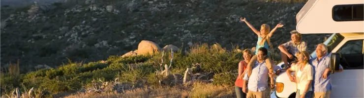 Une famille pose joyeusement devant un camping-car, surplombant un vaste paysage montagneux au coucher du soleil.