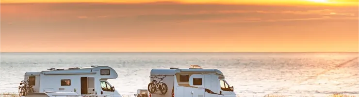 Plusieurs camping-cars sont garés près de la mer au coucher du soleil, créant une scène de voyage et de liberté.