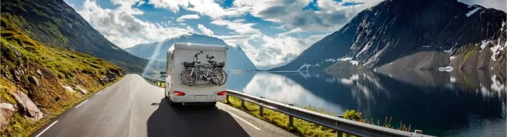 Un camping-car blanc roule sur une route sinueuse le long d'un fleuve, sous un ciel bleu spectaculaire.