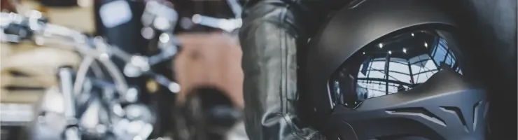 Un motard tenant un casque noir mat avec une visière réfléchissante, prêt à l'aventure devant une moto.