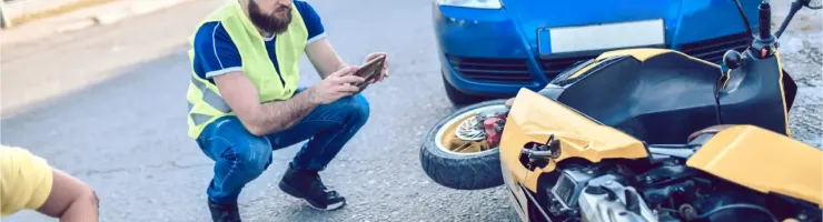 Un homme en gilet de sécurité prend des photos d'un accident impliquant une voiture bleue et une moto jaune au