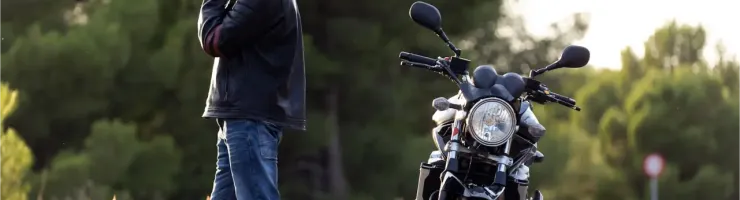 Un motard sur le bord d'une route déserte, parlant au téléphone à côté de sa moto garée, casque au sol.