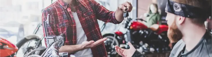 Un vendeur souriant remet les clés d'une moto à un client barbu et tatoué dans un magasin de motos.