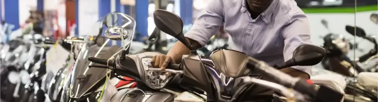 Un homme examine attentivement des scooters dans un magasin de motos, se penchant pour toucher un guidon.