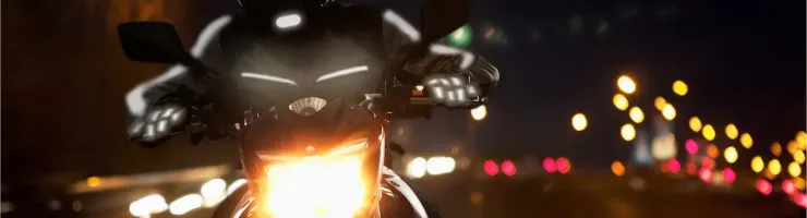 Un motard sur sa moto la nuit, vêtu d'un équipement réfléchissant, avec le phare allumé.
