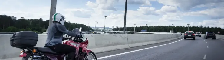 Un motard roule sur une autoroute sous un ciel nuageux, avec une moto équipée de sacoches.