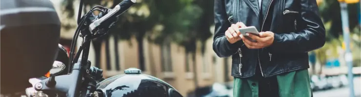 Une femme en blouson de cuir et jean vérifie son téléphone à côté d'une moto Harley-Davidson.