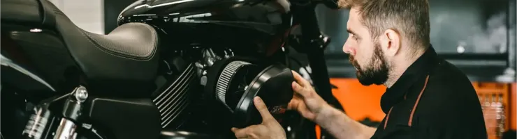 Un homme barbu, mécanicien, travaille sur le moteur d'une moto noire en atelier.