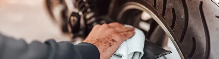 Une main nettoie le pneu arrière d'une moto avec un chiffon blanc et une jante noire.