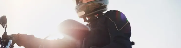 Un motard en tenue de protection et casque intégral regarde vers le ciel sous un soleil éclatant.