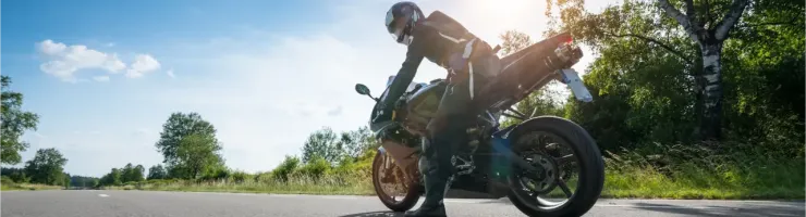 Un motard se penche sur sa moto sportive sur une route de campagne ensoleillée, sous un ciel bleu.