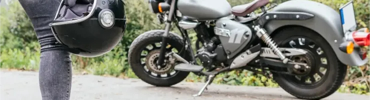 Un motard tenant son casque noir à côté d'une moto custom grise garée sur le côté d'une route.