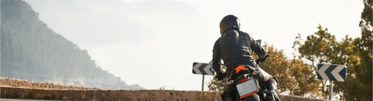Vue arrière d'un motard prenant un virage sur une route de montagne sinueuse, avec des paysages brumeux.