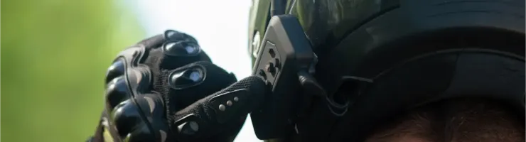 Gros plan sur une main gantée ajustant un intercom sur un casque de moto noir.