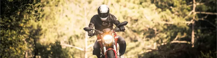 Un motard sur une moto rouge avec un casque blanc prend un virage sur une route de montagne.