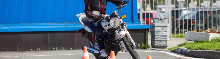 Une femme en casque et équipement de protection pratique la conduite de moto entre des cônes.