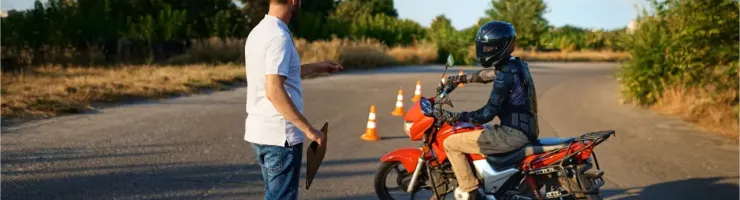 Un instructeur guide un élève motard en casque et équipement sur une moto rouge lors d'un cours.