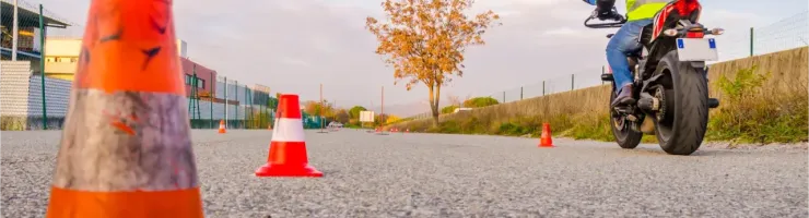 Un motard en gilet jaune fluorescent navigue entre des cônes de signalisation orange sur un terrain d'entra