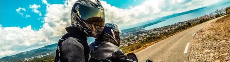 Deux motards en casque admirant la vue sur la mer depuis une route en lacets par temps ensoleillé.