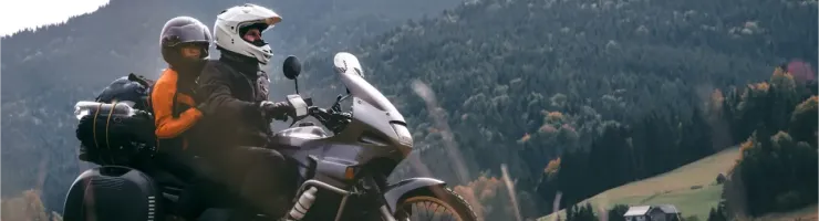 Deux motards avec bagages sur une moto de tourisme dans un paysage montagneux verdoyant et vallonné.