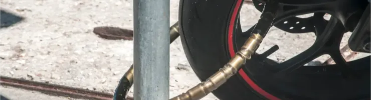 Gros plan d'une chaîne antivol enroulée autour de la roue avant d'une moto et d'un poteau.