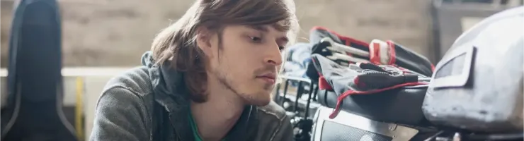 Un jeune homme aux cheveux longs travaille méticuleusement sur les détails d'une moto dans un garage.