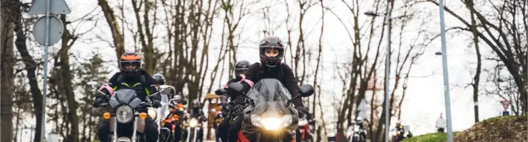 Un groupe de motards casqués roulant sur une route bordée d'arbres dénudés.
